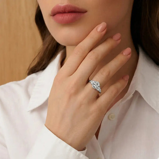 Close-up of a flawless 2-carat silver moissanite ring on a finger, featuring a white embroidered shirt cuff and nude manicure.