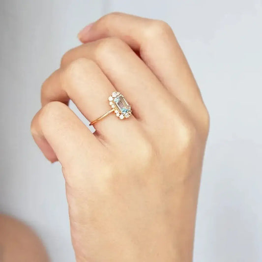 Blue topaz halo ring in 925 silver with a soft warm gold finish worn on a finger to show scale and colour.