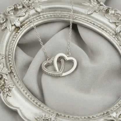 Macro shot of the Moissanite Interlocking Heart Necklace on an grey satin background, showing the intricate pavé detail and high-polish finish.