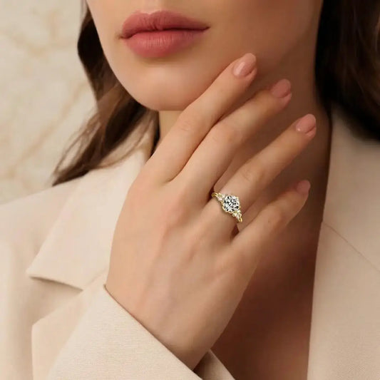 Close-up of a yellow gold moissanite ring on a finger, featuring a beige embroidered blaser cuff and nude manicure.