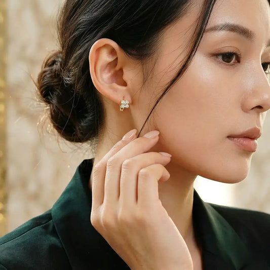 An elegant model with an updo hairstyle wearing gold hoop earrings with shimmering moissanite clovers.