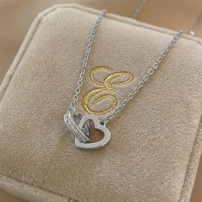 Sterling silver interlocking heart pendant with VVS moissanite stones resting on a luxurious beige silk fabric.
