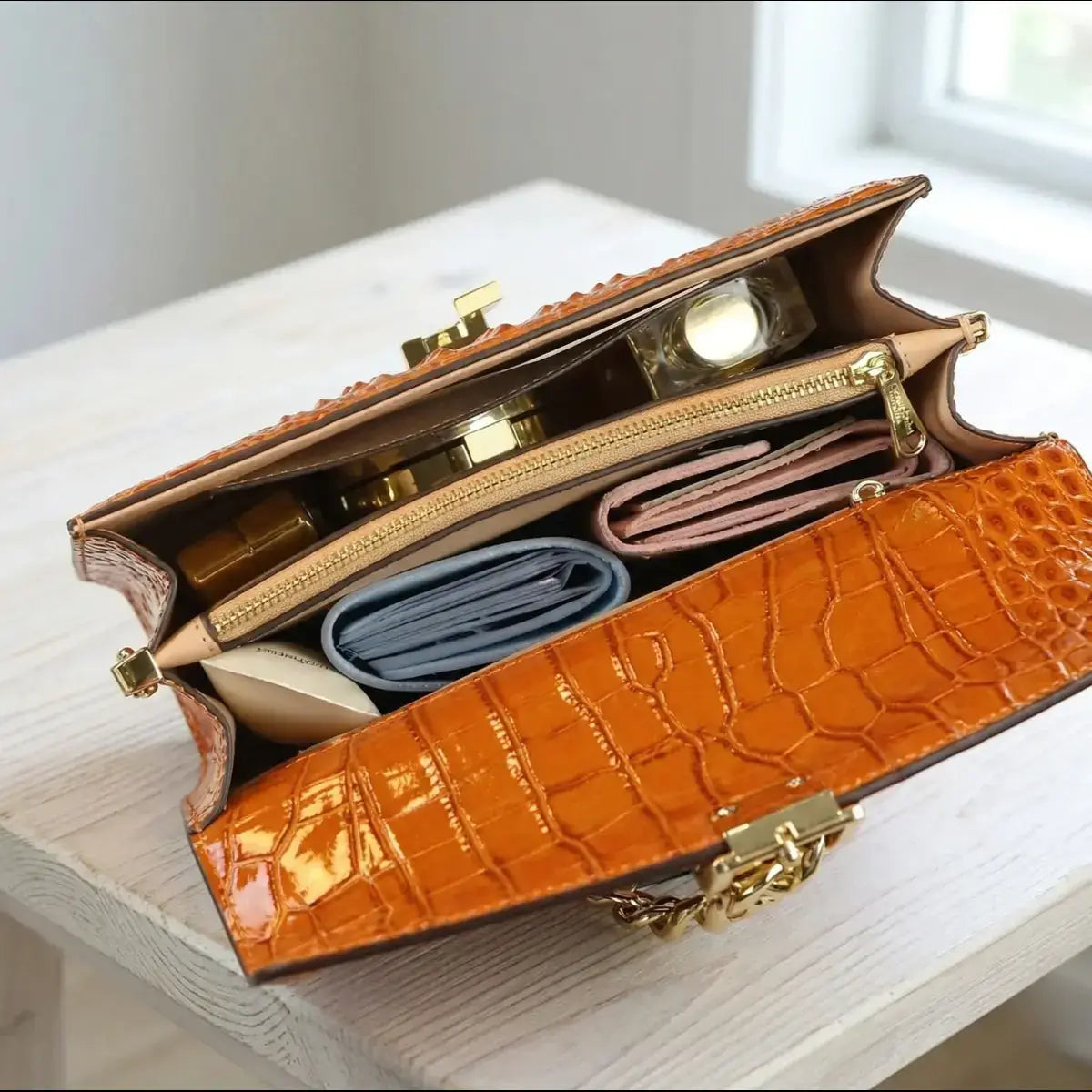 Interior of the open Orange Leather Crossbody Handbag, showing the spacious compartments, zipped dividers, and personal items like a wallet and cosmetics.